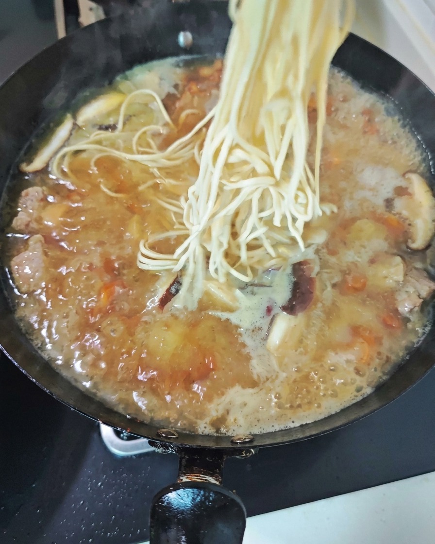 Un nid de nouilles fraîches et claires plongé dans un wok bouillonnant de soupe de poulet savoureuse garnie de tranches de champignons.