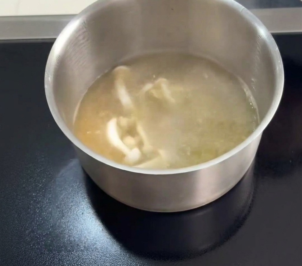 Des champignons jade blanche et de fines fleurs de cordyceps orange ajoutés à un bouillon de poulet clair en ébullition.