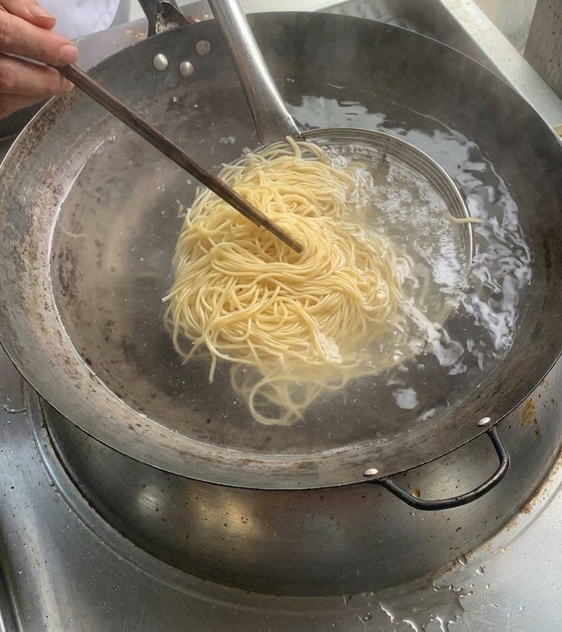 Nouilles cuites maintenues dans une passoire métallique au-dessus dune casserole deau bouillante.