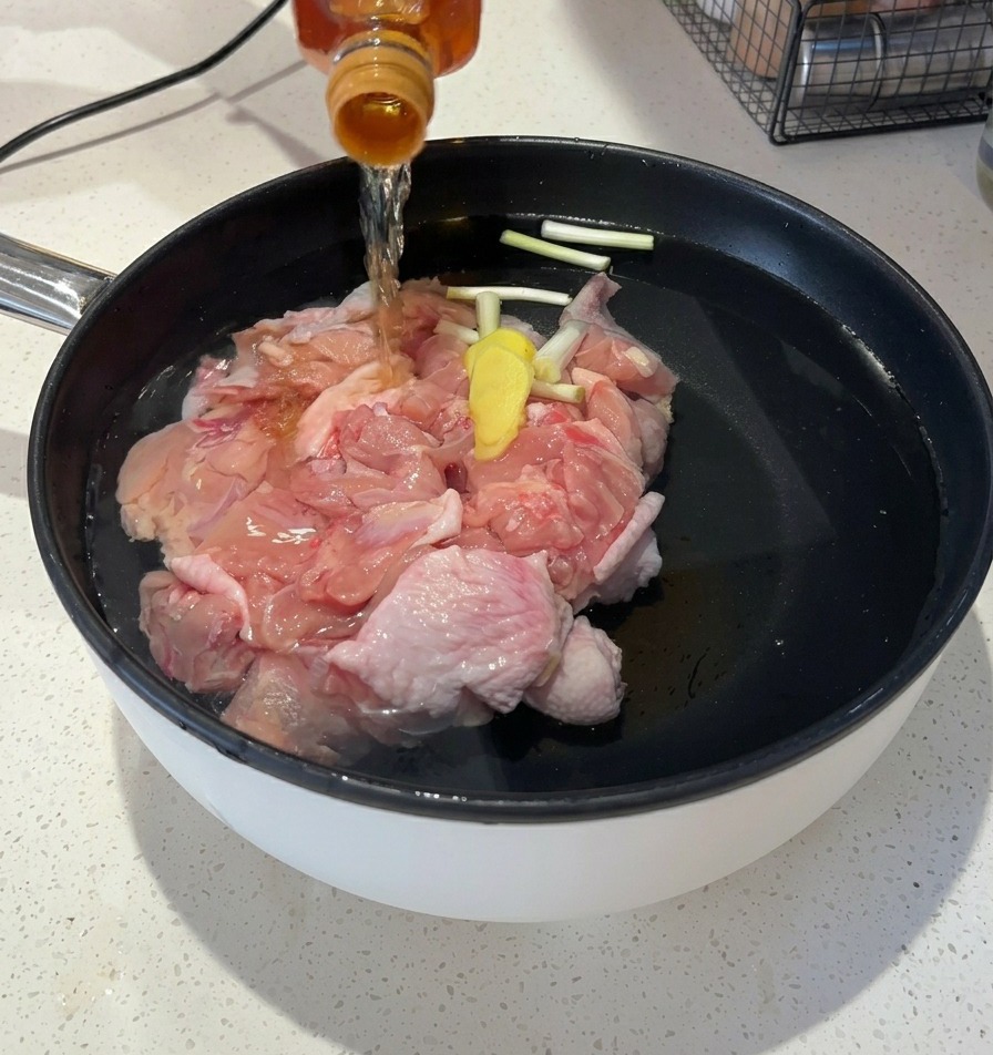 Verser un liquide ambré clair dune bouteille en verre dans la casserole deau avec le poulet.