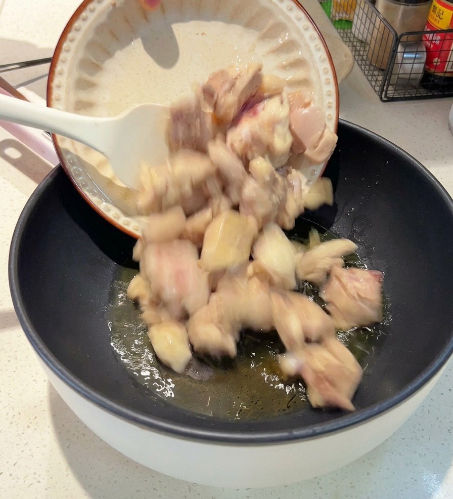 Une assiette blanche versant des morceaux de poulet blanchis dans une poêle sombre contenant de lhuile chaude.