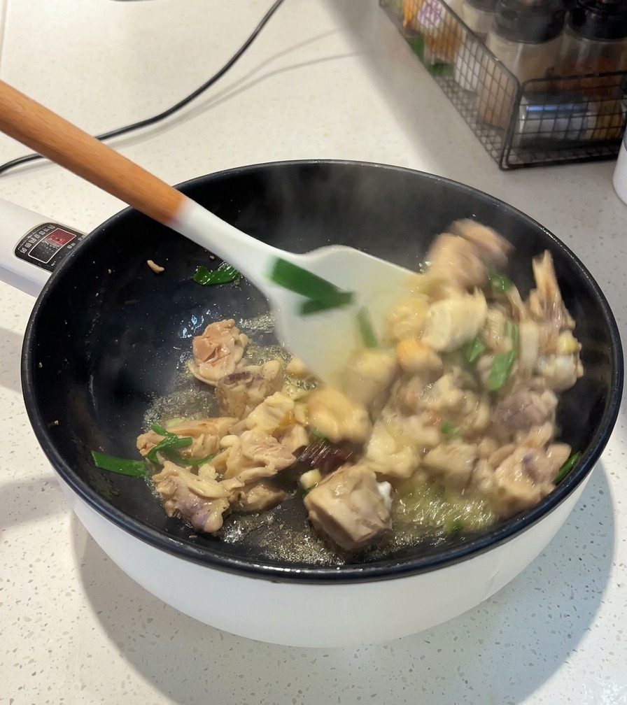 Une spatule blanche remuant les morceaux de poulet, les oignons verts et lanis étoilé dans une poêle sur le feu.