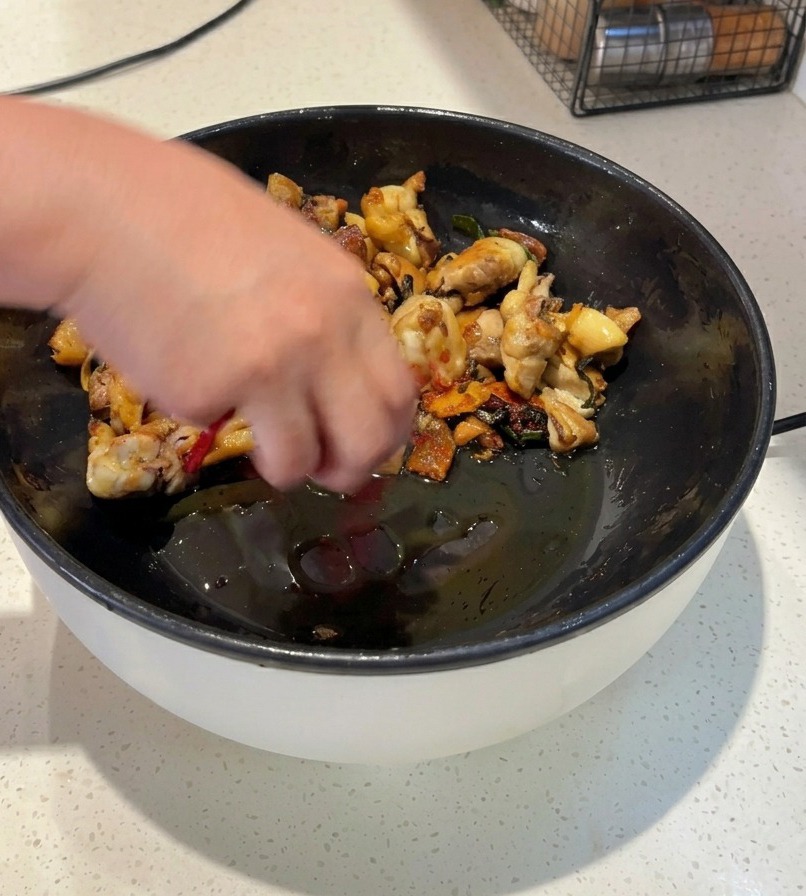 Une personne faisant sauter du poulet dans une poêle noire avec des piments rouges séchés entiers et de la poudre de piment rouge vif.