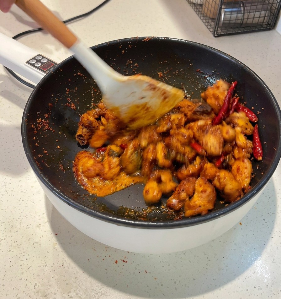 Une spatule blanche mélangeant des morceaux de poulet dans une sauce rouge foncé jusquà ce que chaque morceau soit enrobé.
