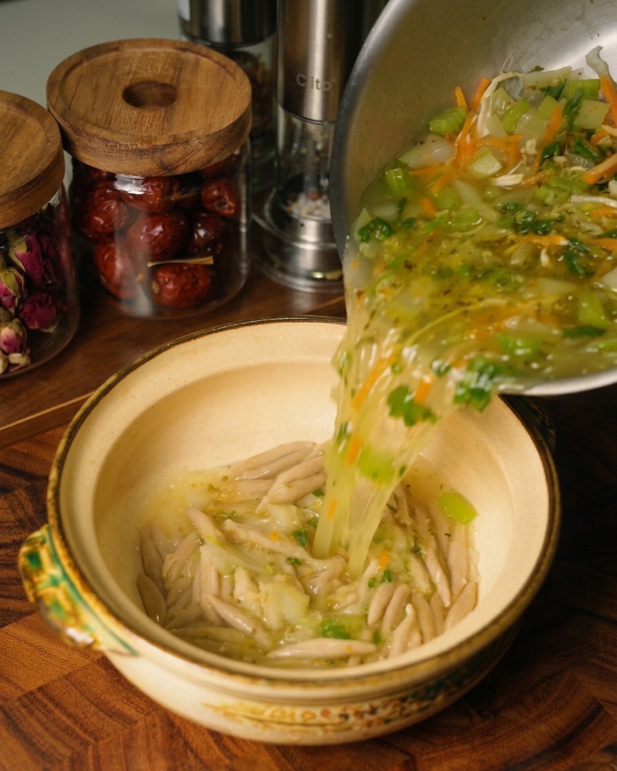 Une soupe chaude au poulet et aux légumes versée depuis une marmite en acier inoxydable dans un bol en céramique contenant les nouilles davoine cuites.