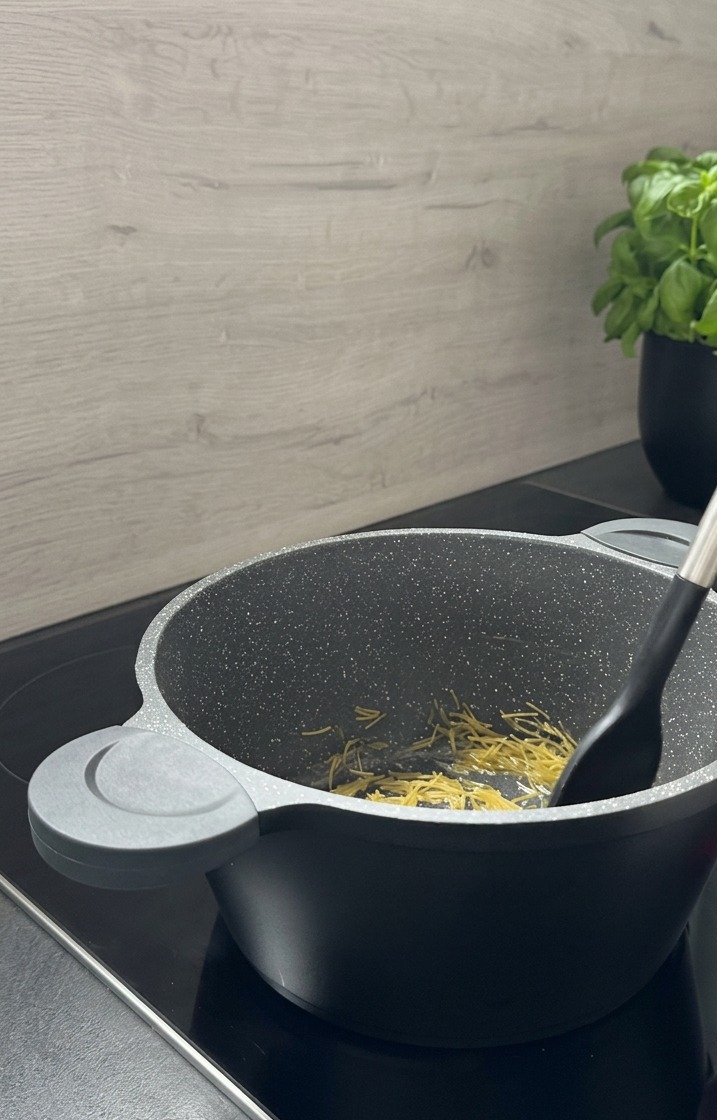 Des petites pâtes langues doiseau remuées avec une spatule noire dans une marmite grise effet granit pendant quelles dorent.