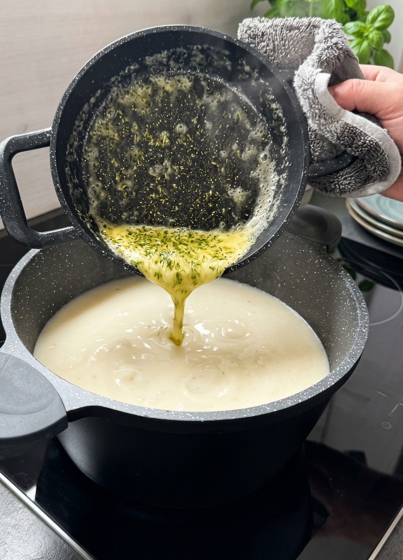 Du beurre jaune fondu avec des flocons de menthe séchée verte versé dune petite casserole noire dans une soupe blanche crémeuse.