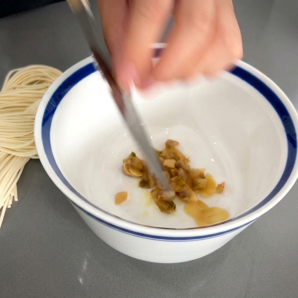 La lame dun couteau faisant glisser des légumes saumurés émincés de couleur brune dans un bol blanc contenant déjà lail et lassaisonnement.
