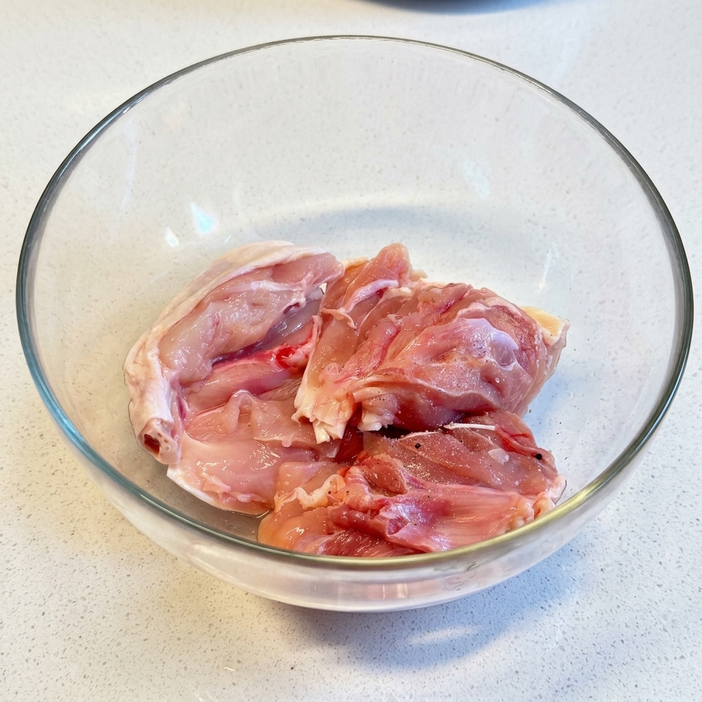 Hauts de cuisse de poulet crus assaisonnés de sel et de poivre dans un saladier en verre transparent.
