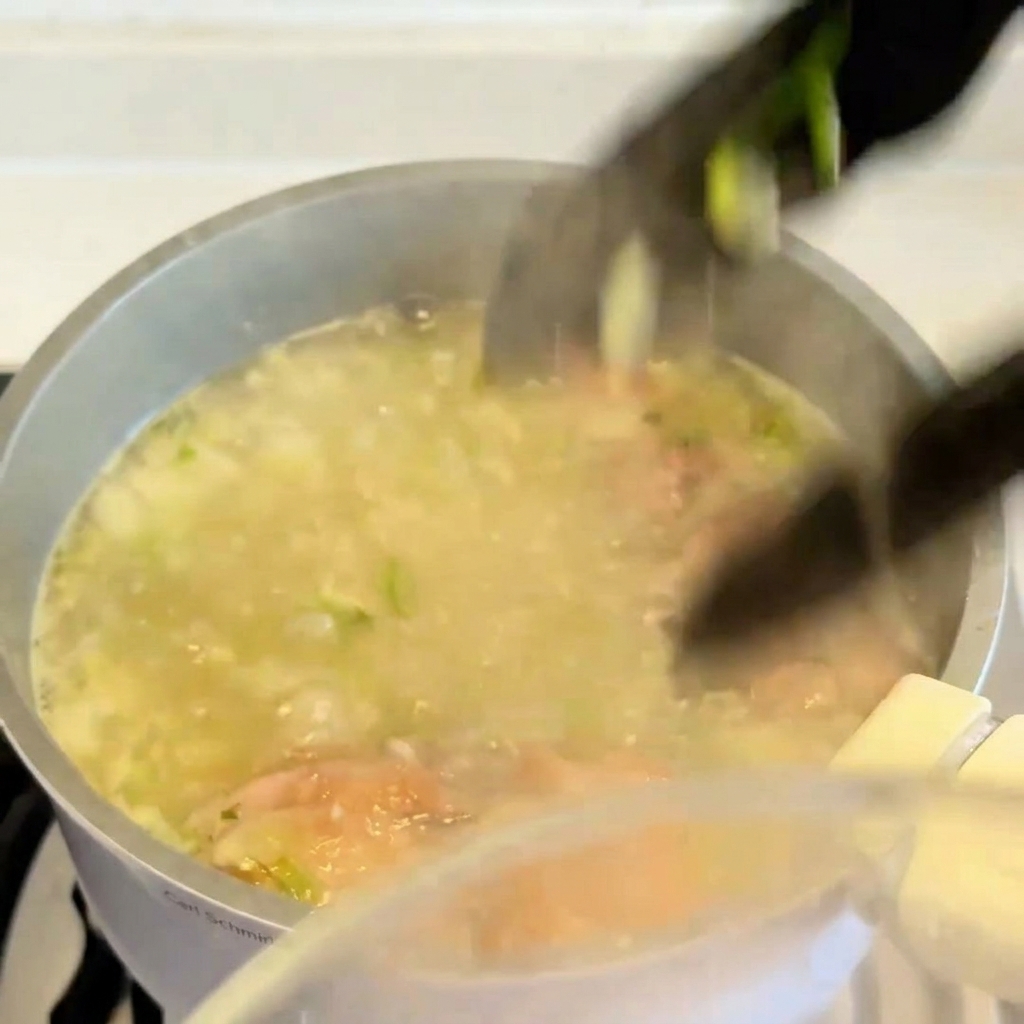 Une pince de cuisine soulevant un haut de cuisse de poulet cuit et doré hors dune marmite de bouillon frémissant.