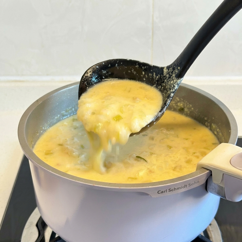 Une louche noire soulevant une portion de soupe grecque au poulet et au citron, devenue épaisse et dun jaune crémeux.