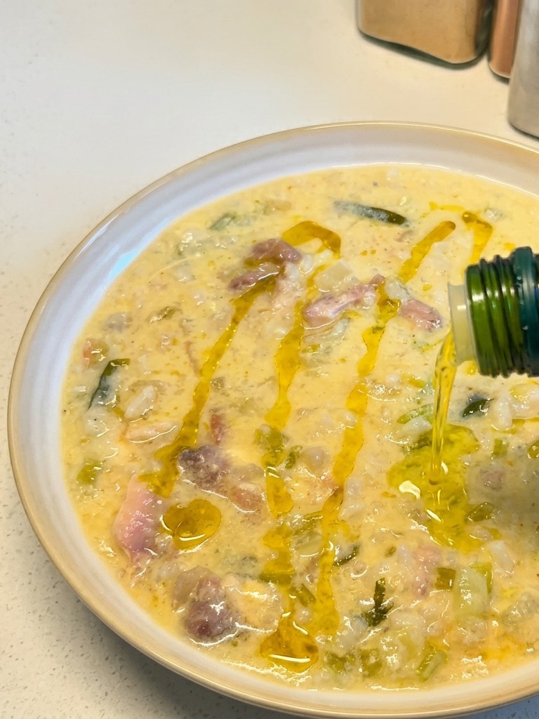Huile dolive dorée versée dune bouteille verte sur un bol de soupe crémeuse au poulet et au citron.