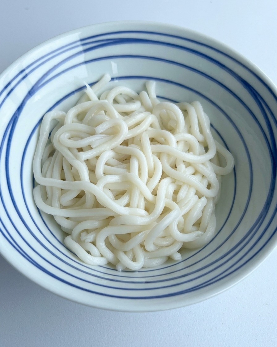 Sauce soja foncée et assaisonnements versés sur un nid dudon blanches dans un bol à rayures bleues.