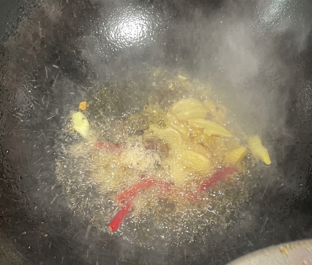 Des tranches de gingembre et des piments rouges séchés crépitant dans lhuile chaude au fond dun wok sombre.