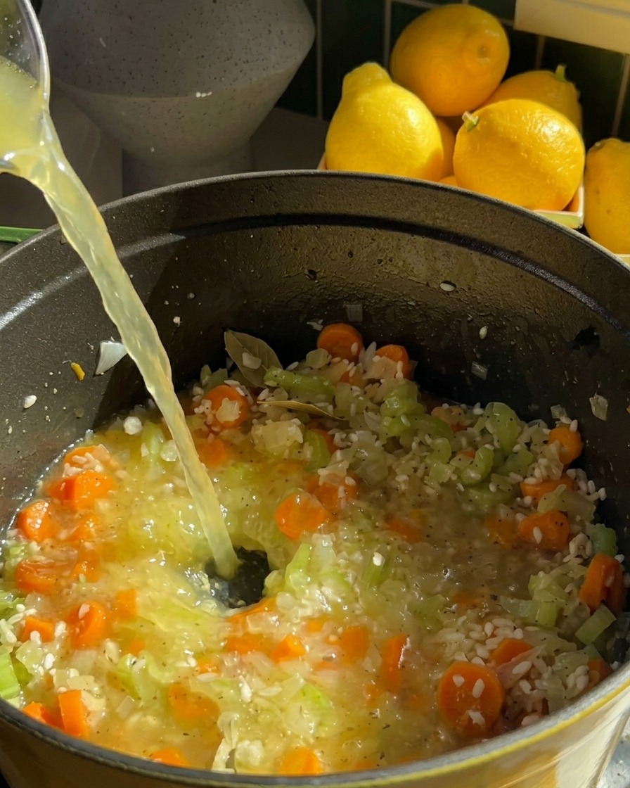 Un filet de bouillon de poulet clair versé dans une marmite contenant du riz, des carottes et du céleri.