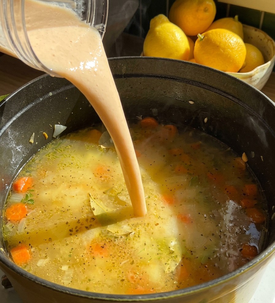 Un filet de purée de haricots beige et crémeuse versé depuis le blender dans une marmite de soupe frémissante avec des carottes.