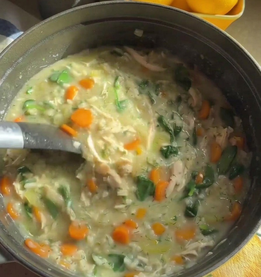 Une louche en métal remuant une soupe crémeuse et épaisse au poulet, garnie de carottes orange et dépinards verts.
