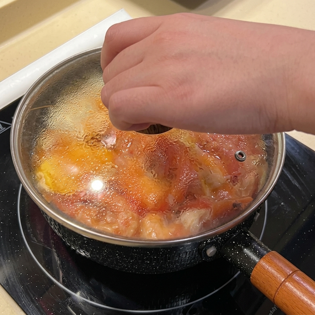 Une main posant un couvercle en verre transparent sur une casserole noire remplie de nouilles, dœufs et de crevettes.