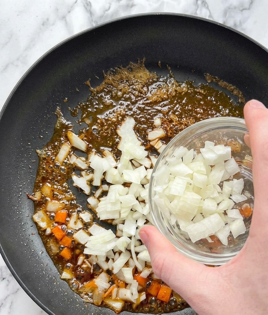 Des oignons blancs coupés en dés versés dun bol en verre dans une poêle contenant les sucs de cuisson du saumon et du beurre.