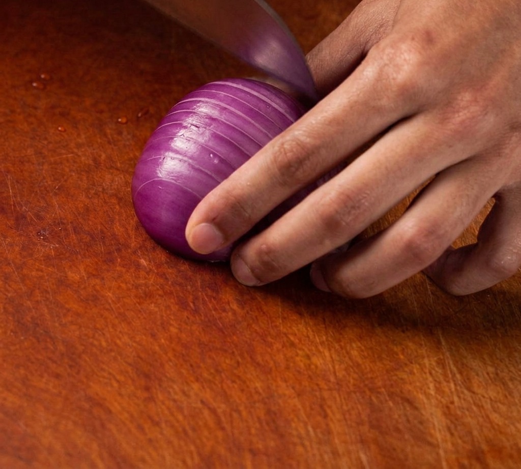 Un couteau bien aiguisé coupant un oignon rouge en petits dés réguliers sur une planche en bois.