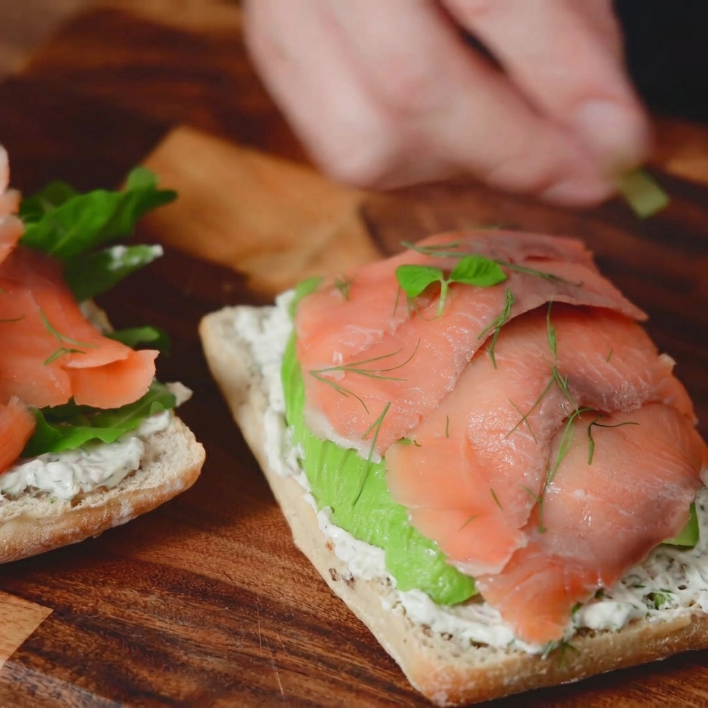 Photographie macro de brins daneth frais et de jeunes pousses ajoutés en garniture au-dessus dun sandwich au saumon fumé.