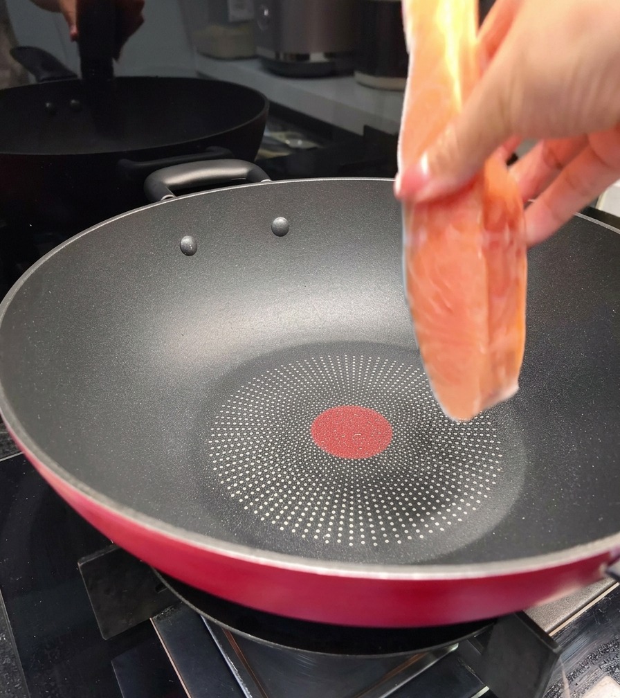 Une main déposant un pavé de saumon frais dans une grande poêle antiadhésive noire sur une cuisinière.