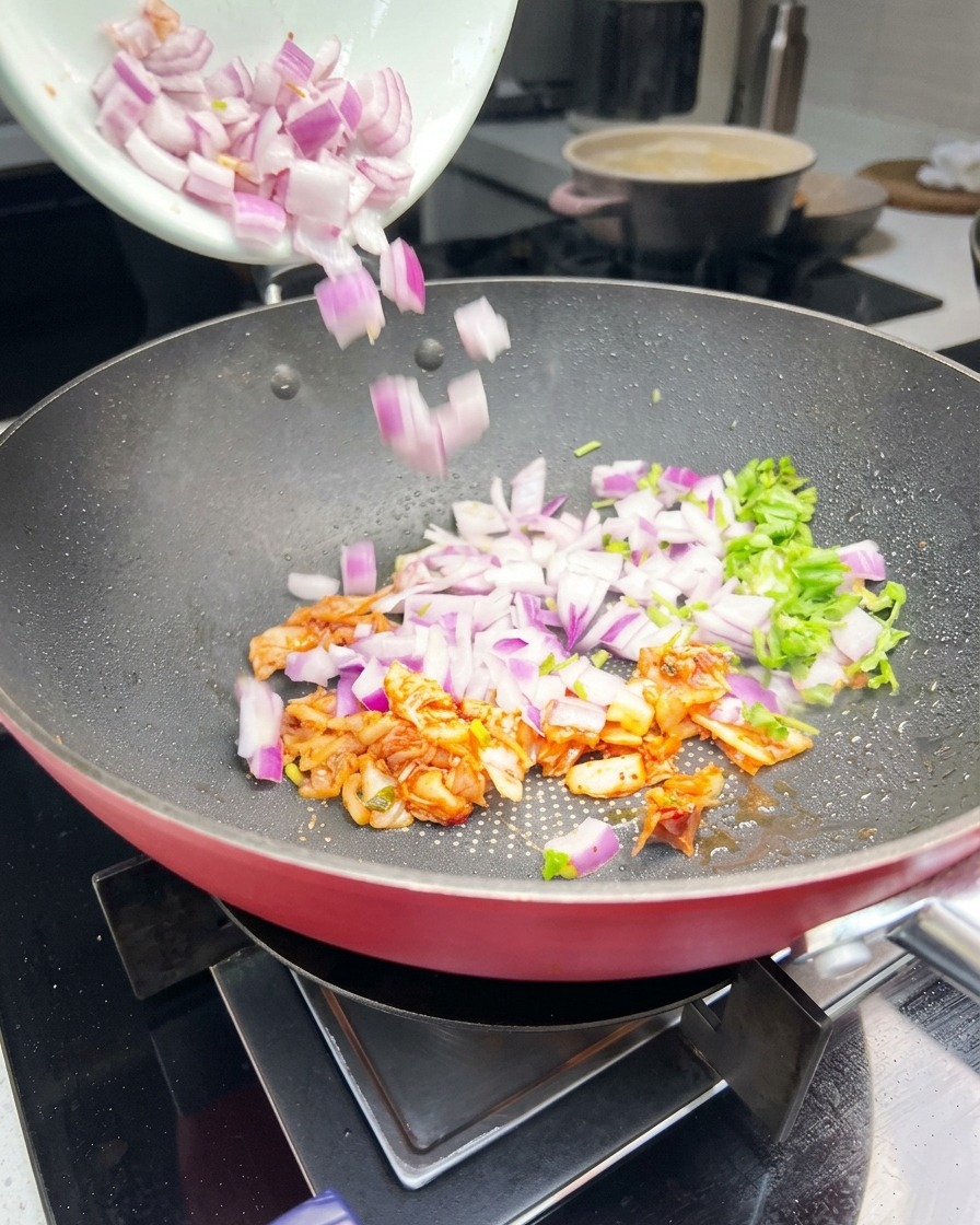 Des oignons violets émincés, de la coriandre verte et du kimchi orange remués dans une poêle.