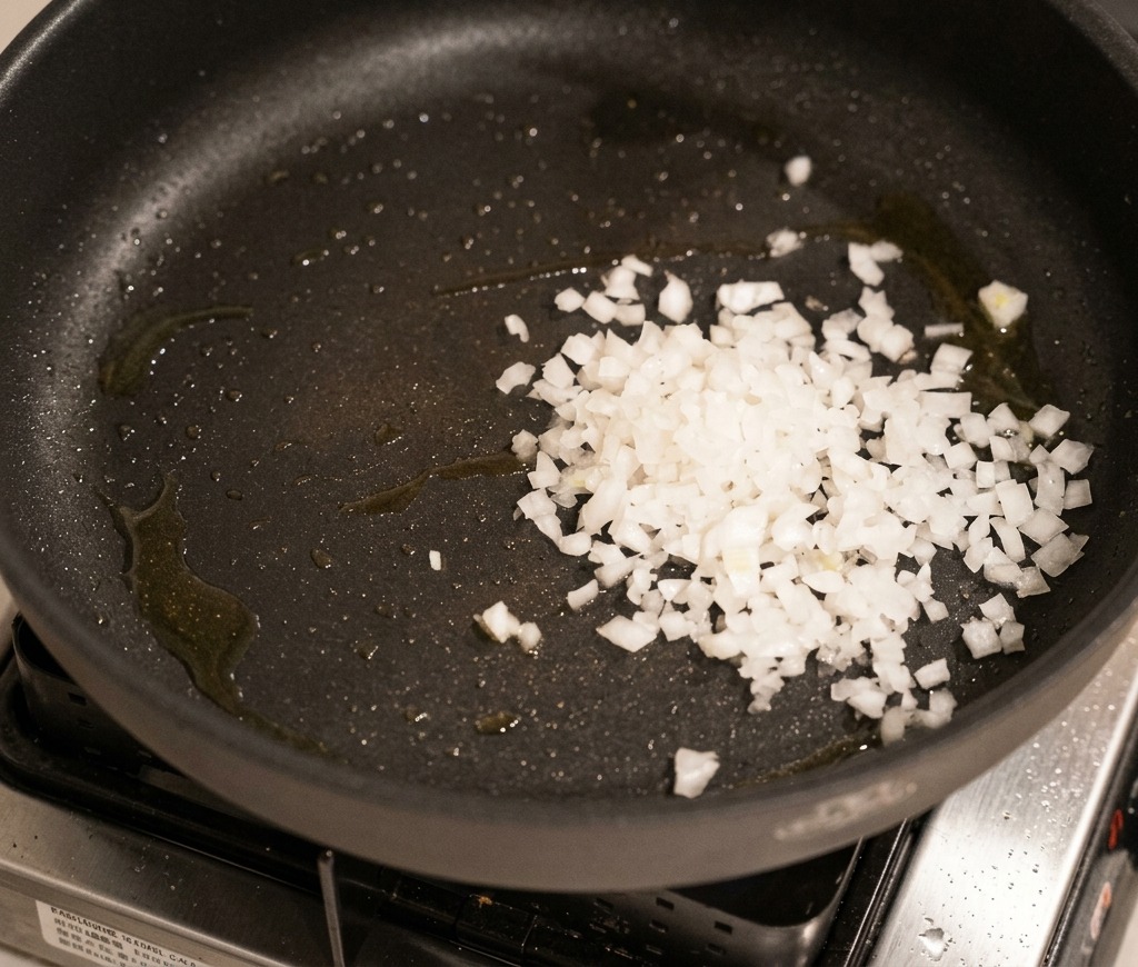 Oignons blancs émincés qui suent doucement dans une poêle sombre jusquà devenir translucides.