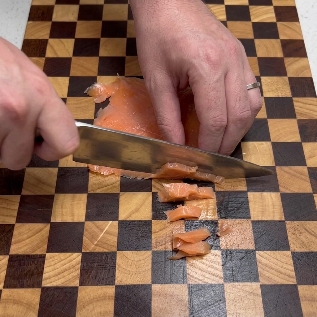 Les mains dun chef coupant des tranches de saumon fumé en petits carrés à laide dun couteau sur une planche à découper.