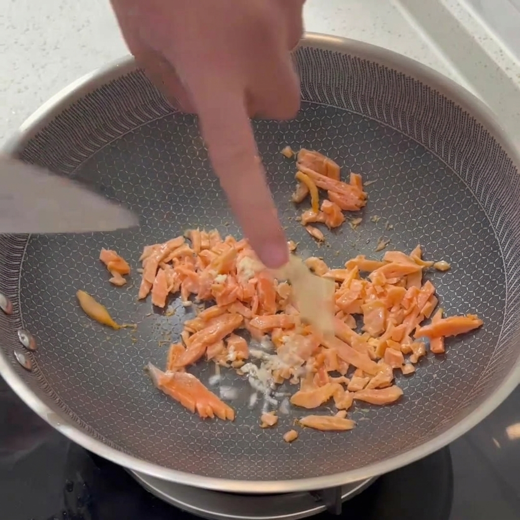 De lail émincé incorporé à laide dune spatule dans une poêle contenant des morceaux de saumon fumé.