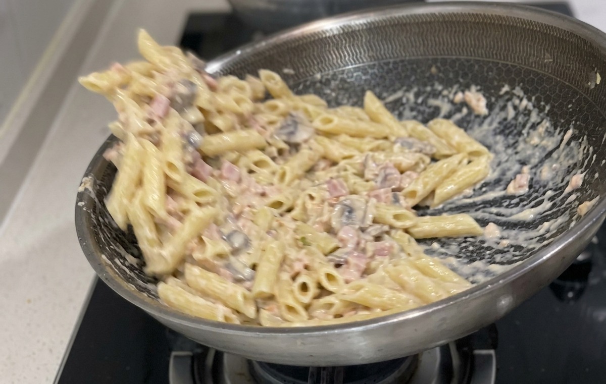 Des penne cuites mélangées et enrobées de sauce crème et de morceaux de saumon dans une grande poêle.