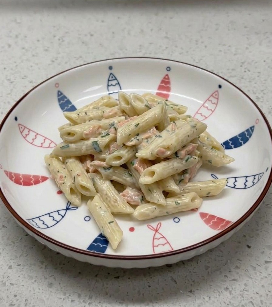 Une portion de penne crémeuses au saumon dressée dans un bol en céramique blanche orné de motifs de poissons.