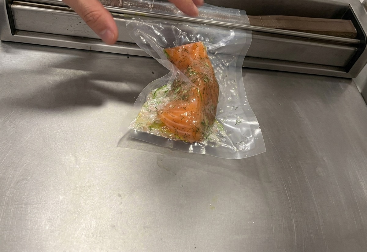 Une machine de mise sous vide aspirant lair dun sac plastique contenant le filet de saumon enrobé dherbes.
