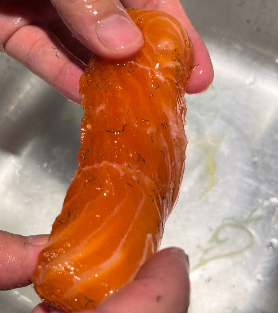 Une main maintenant un filet de saumon sous un filet deau courante pour éliminer le mélange de sel et dépices.