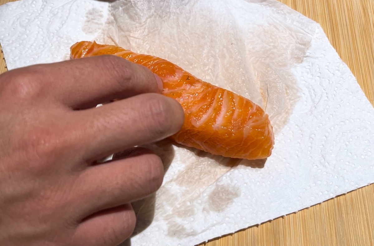 Une main tamponnant un filet de saumon orange éclatant avec du papier absorbant blanc sur une planche en bois.