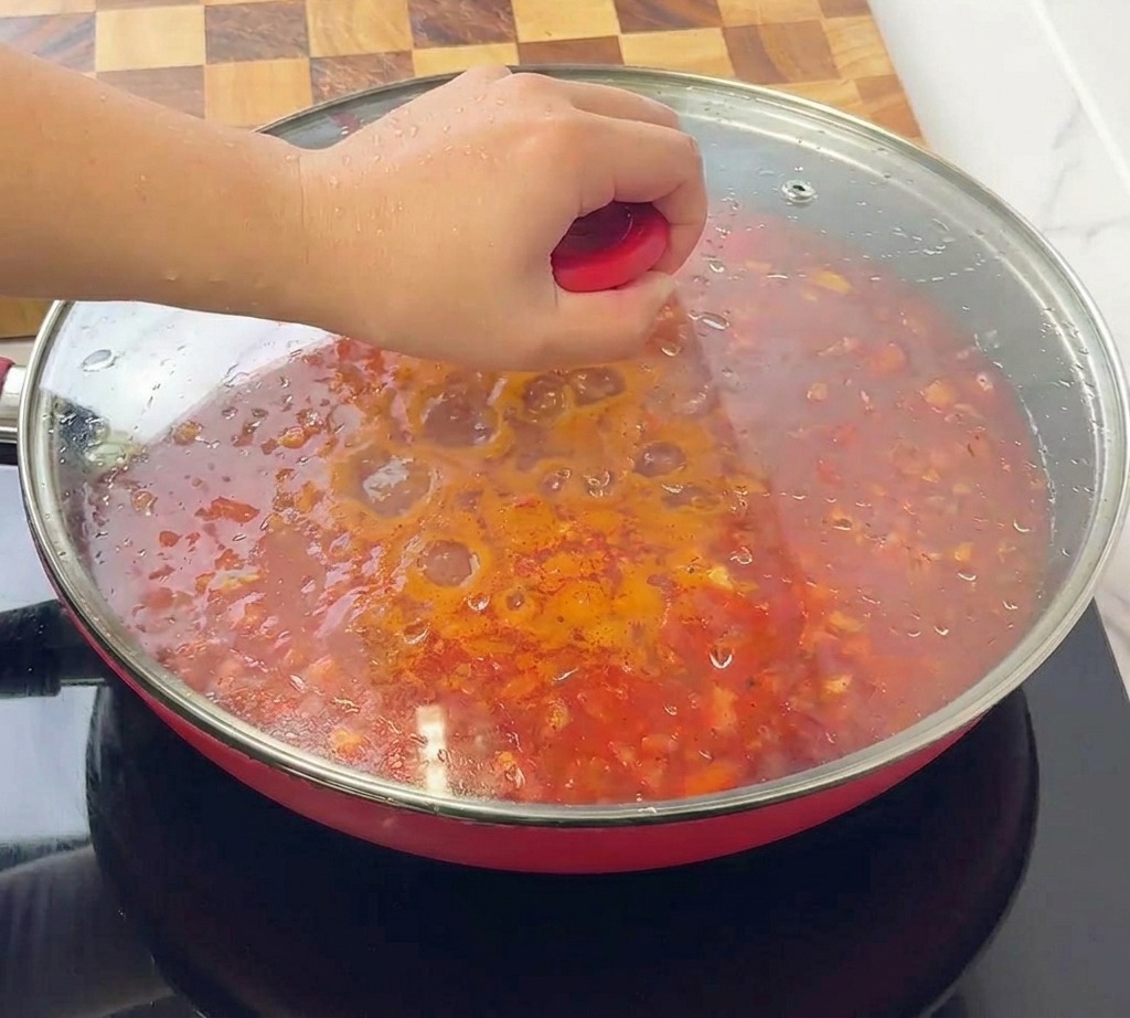 Une personne posant un couvercle en verre transparent sur une sauteuse rouge remplie de sauce bolognaise.