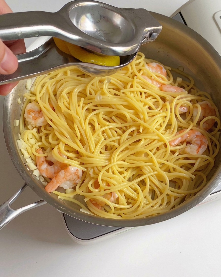Du jus de citron frais pressé à laide dun presse-agrume en métal sur une poêle de crevettes et de spaghetti cuits.