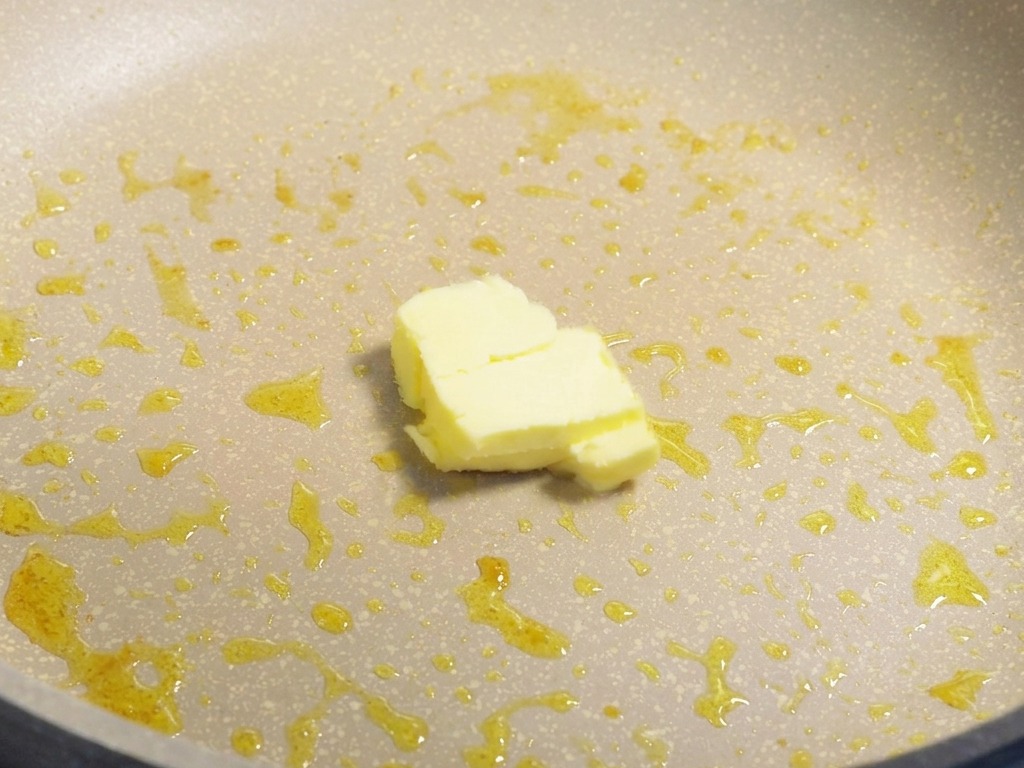 Un petit morceau de beurre jaune fondant dans une poêle avec des sucs de cuisson de crevettes.