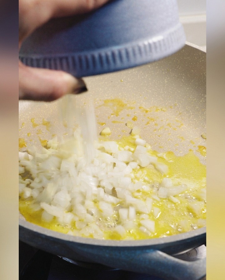 Dés doignon blanc ajoutés depuis un bol bleu dans une poêle de beurre fondu.
