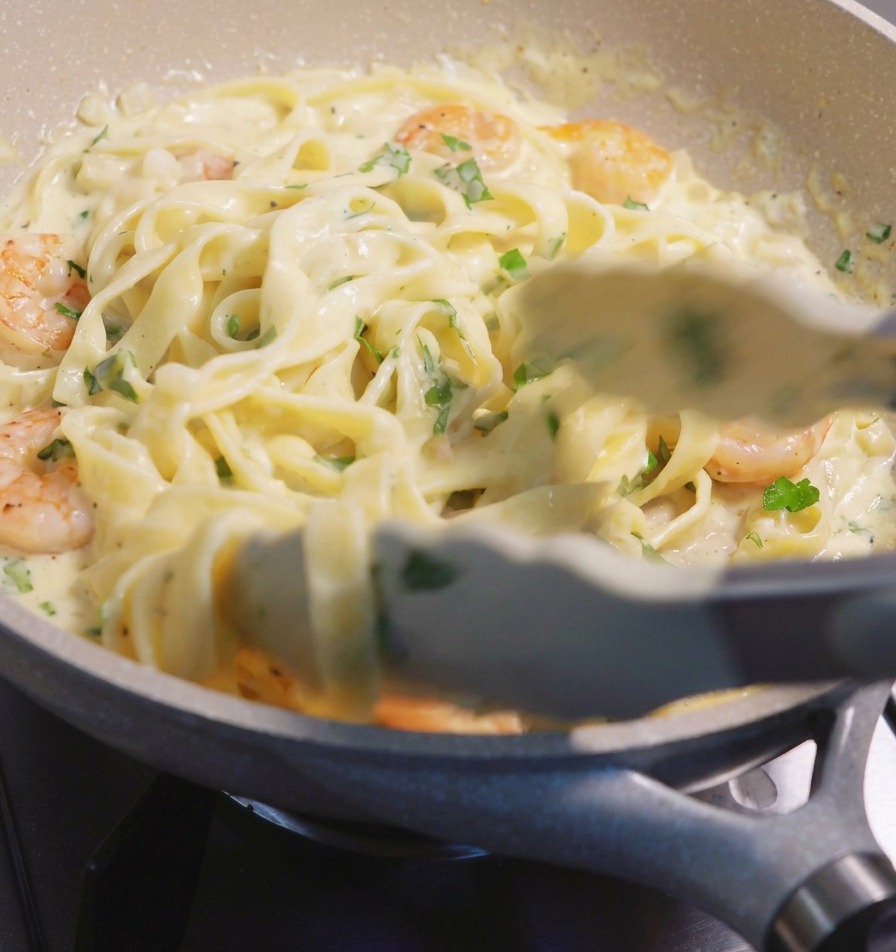Utilisation dune pince pour soulever et mélanger les fettuccine et les crevettes dans une sauce crémeuse.