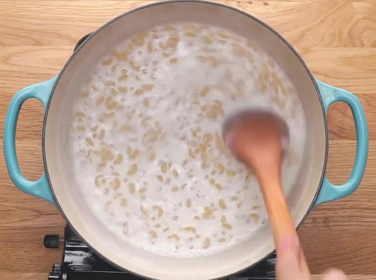 Une cuillère en bois remuant des macaronis qui frémissent dans du lait.