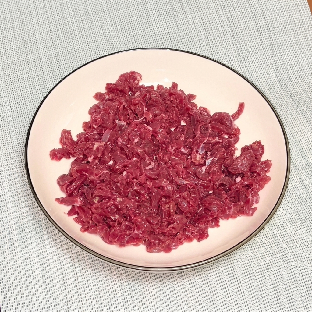 Bœuf haché cru dans un bol blanc saupoudré de poivre noir et dhuile pour la marinade.