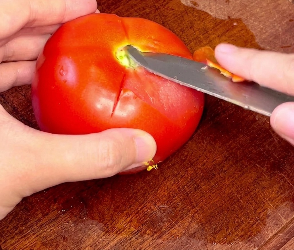 Des mains retirant délicatement la peau dune tomate entière préalablement plongée dans leau chaude à laide dun couteau doffice.