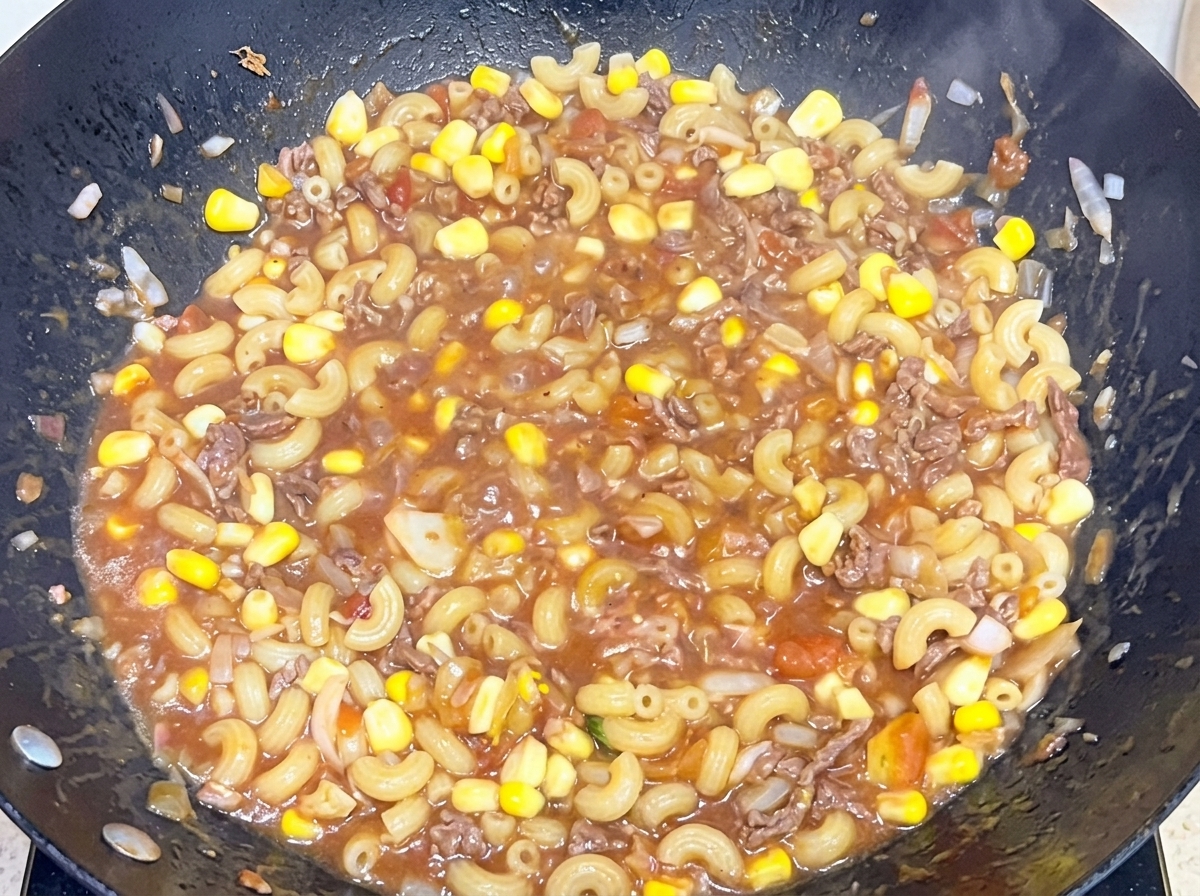 Macaronis cuits mélangés à une sauce savoureuse au bœuf et à la tomate dans un grand wok.