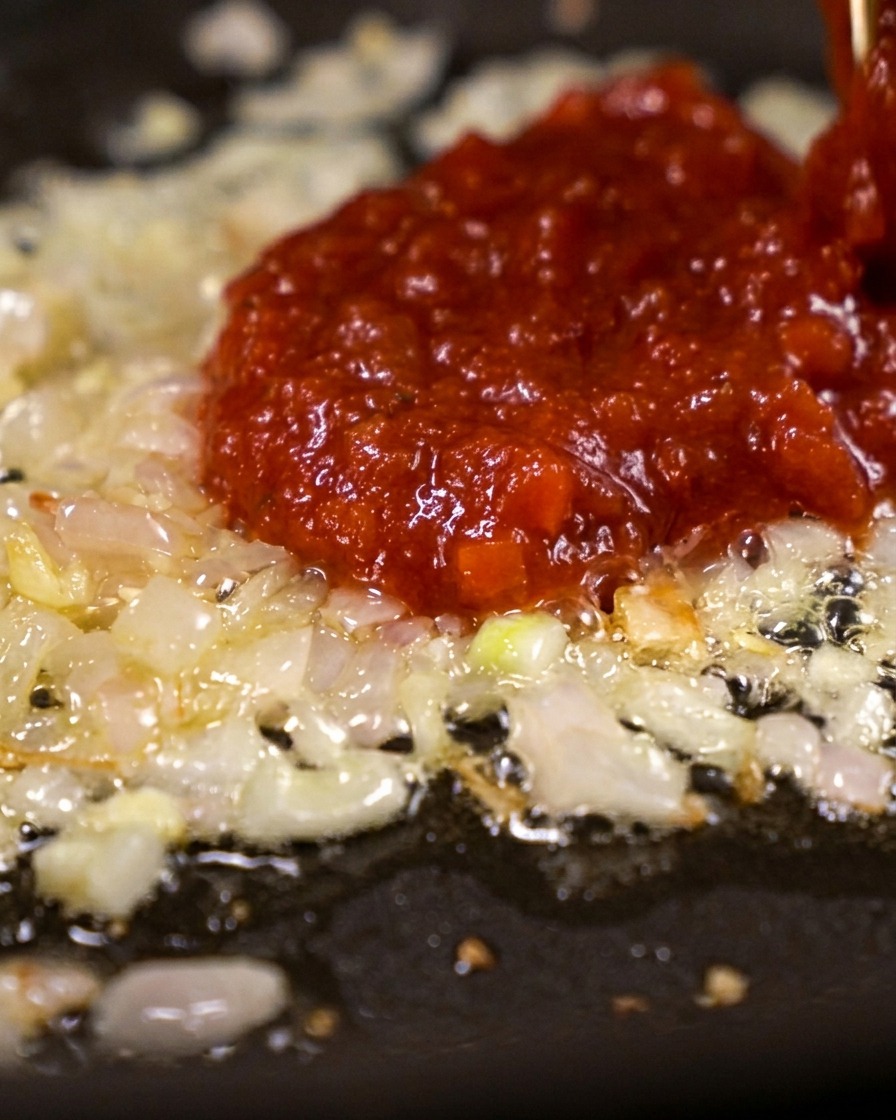 Une grande cuillère de concentré de tomate rouge vif déposée sur un lit déchalotes revenues.
