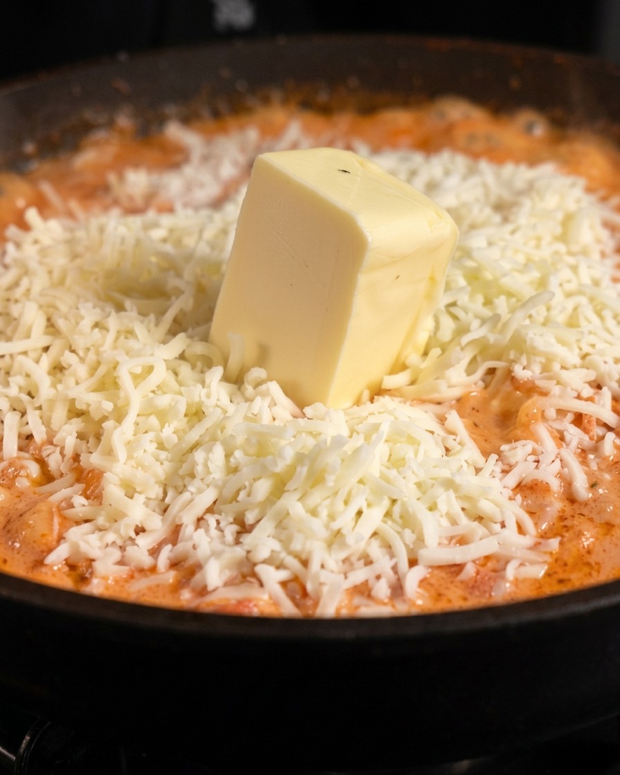 Un morceau épais de beurre posé sur un dôme de mozzarella râpée blanche par-dessus des pâtes en sauce orangée.