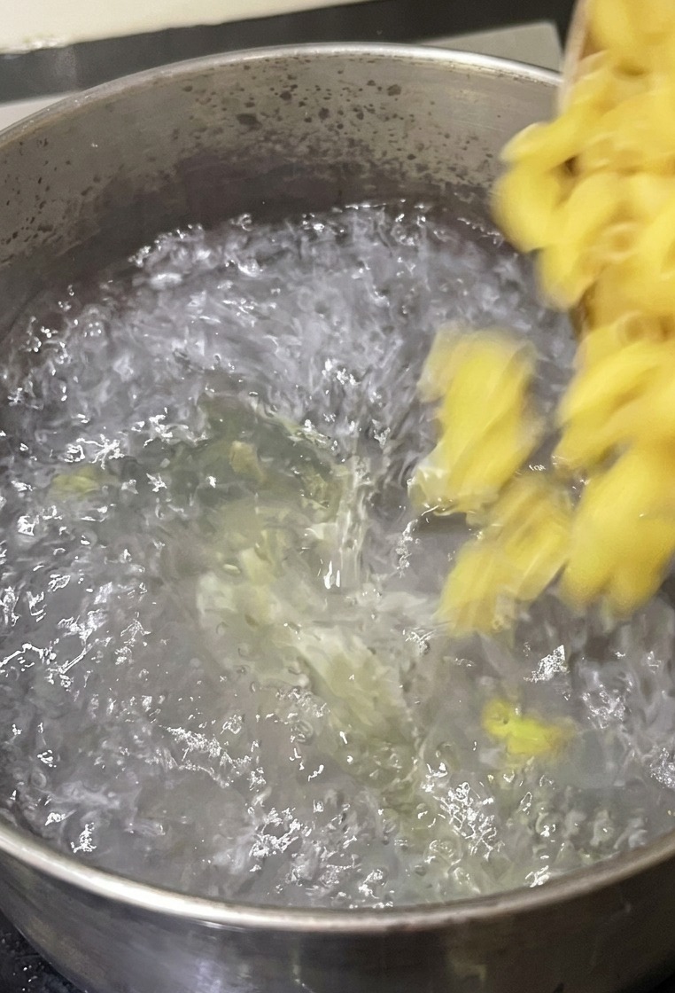 Des macaronis versés depuis un bol dans une casserole en acier inoxydable remplie deau bouillante sur une cuisinière.