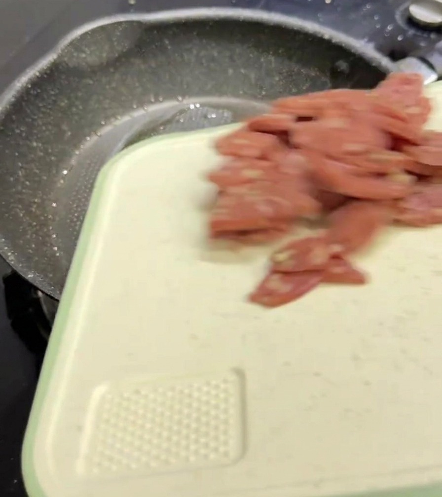 Des tranches de salami rose tombant dune planche à découper blanche dans une poêle à frire sombre et mouchetée.