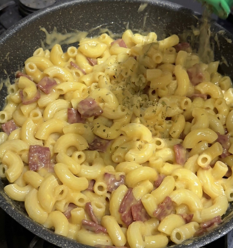 Des flocons de persil vert séché saupoudrés depuis un flacon dépices vert sur une poêle remplie de macaroni au fromage.