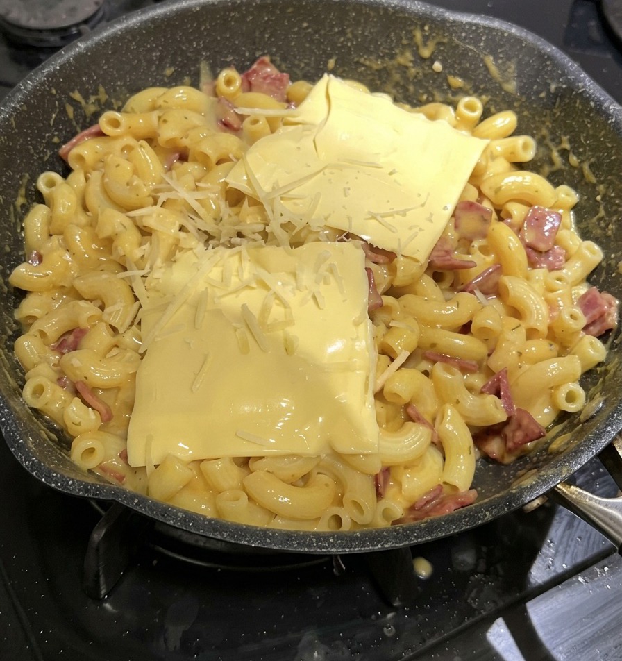 Deux tranches de fromage fondu jaunes carrées et du fromage râpé déposés sur le dessus dune poêle de macaroni au fromage.